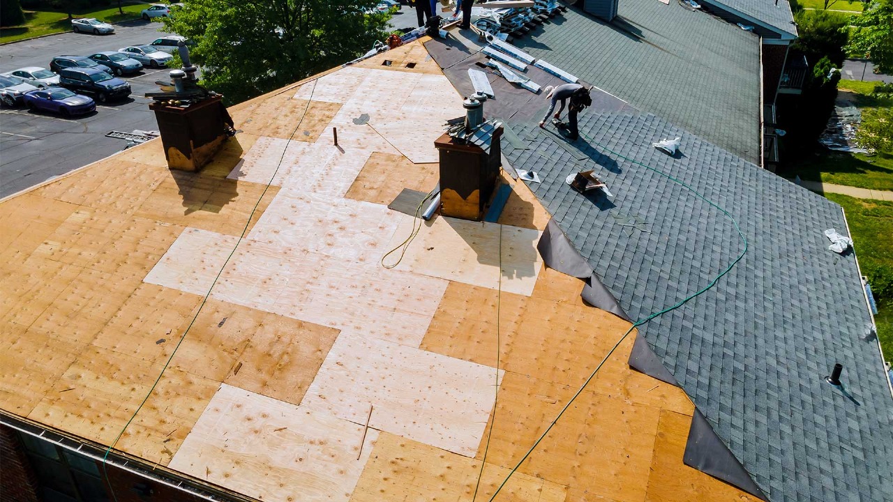 Aerial view of a roof replacement in progress, showing new shingles and exposed plywood